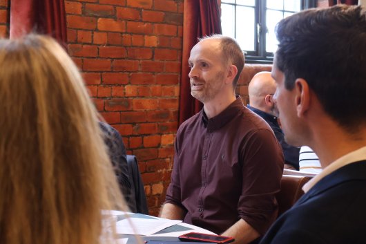 A person in conversation with others at a roundtable